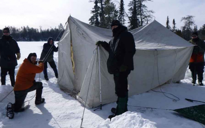 a group of gap year students work to set up a tent on a frozen, snowy lake